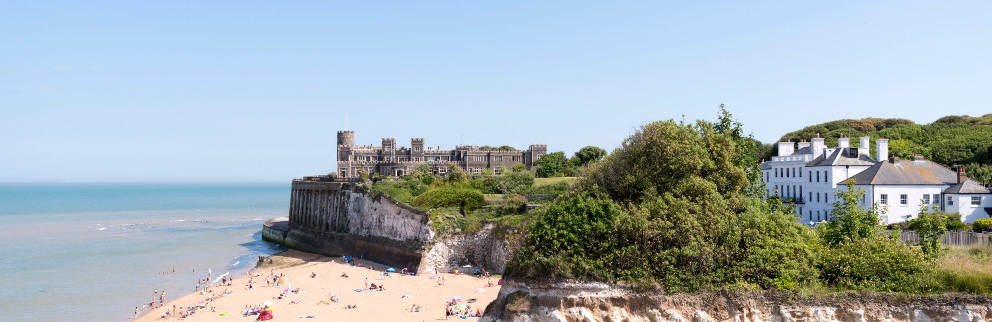 Wide sandy beach and cliffs, gentle waves, and people enjoying the sun