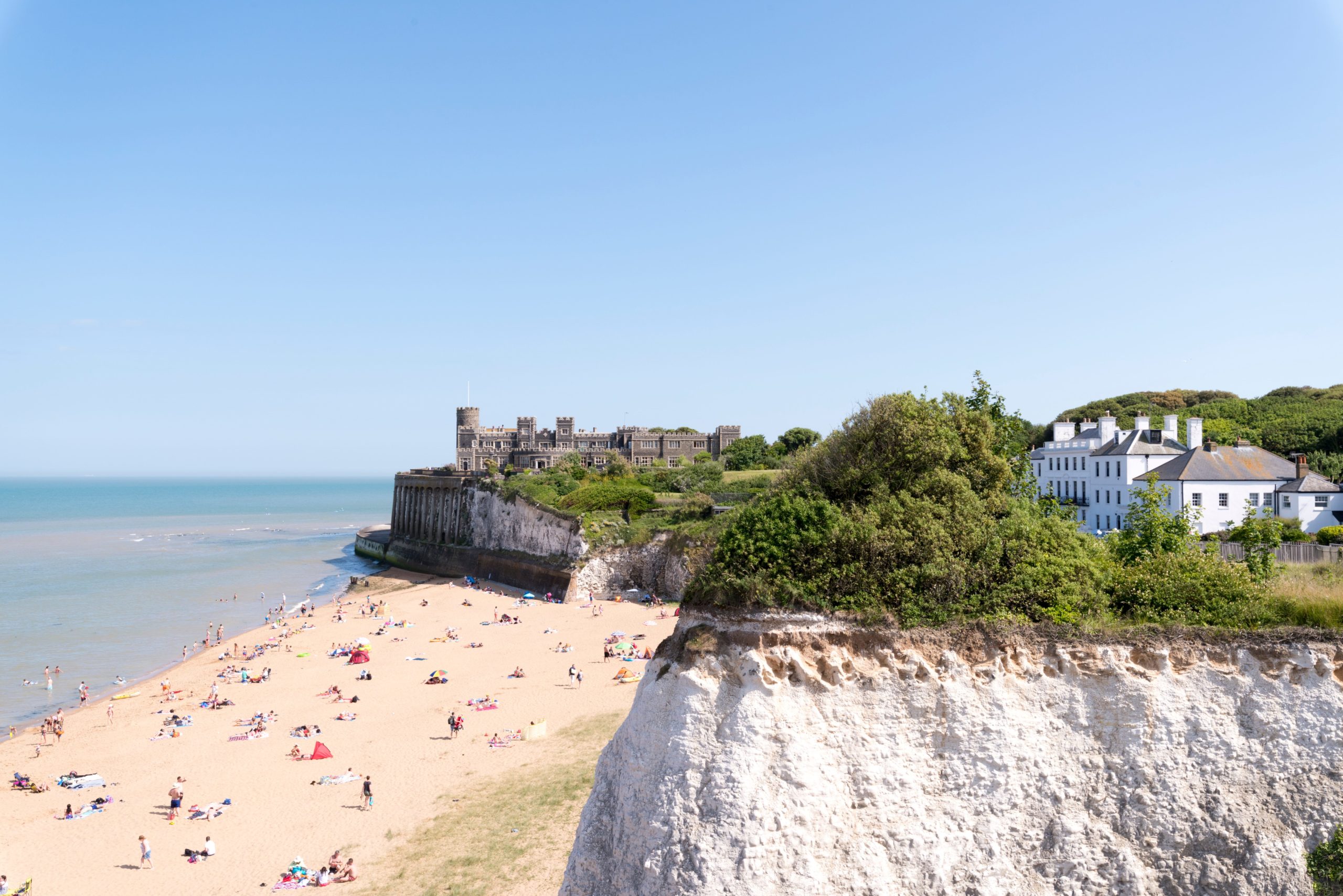 Wide sandy beach and cliffs, gentle waves, and people enjoying the sun