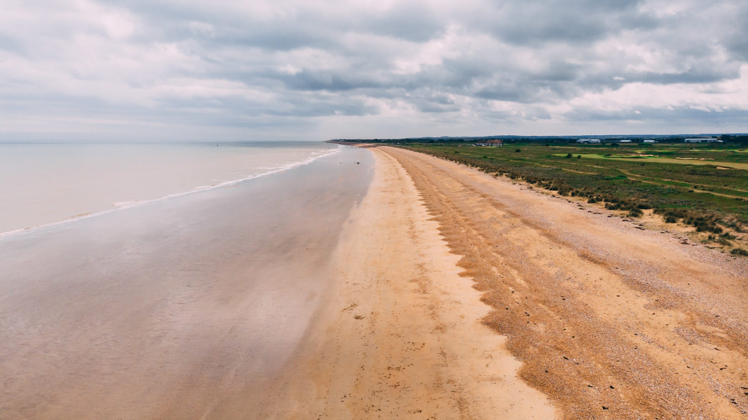 Expansive beach with sand and shingle, calm sea, and grassy dunes in the distance