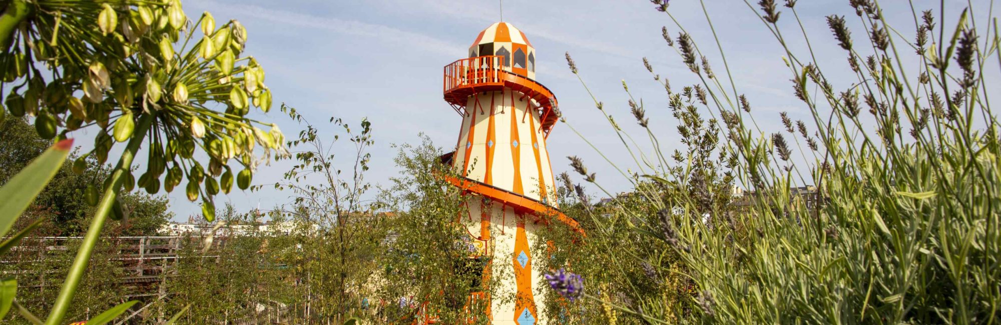 A vintage orange and white helter-skelter peeks through lush greenery at Dreamland Margate on a sunny day.
