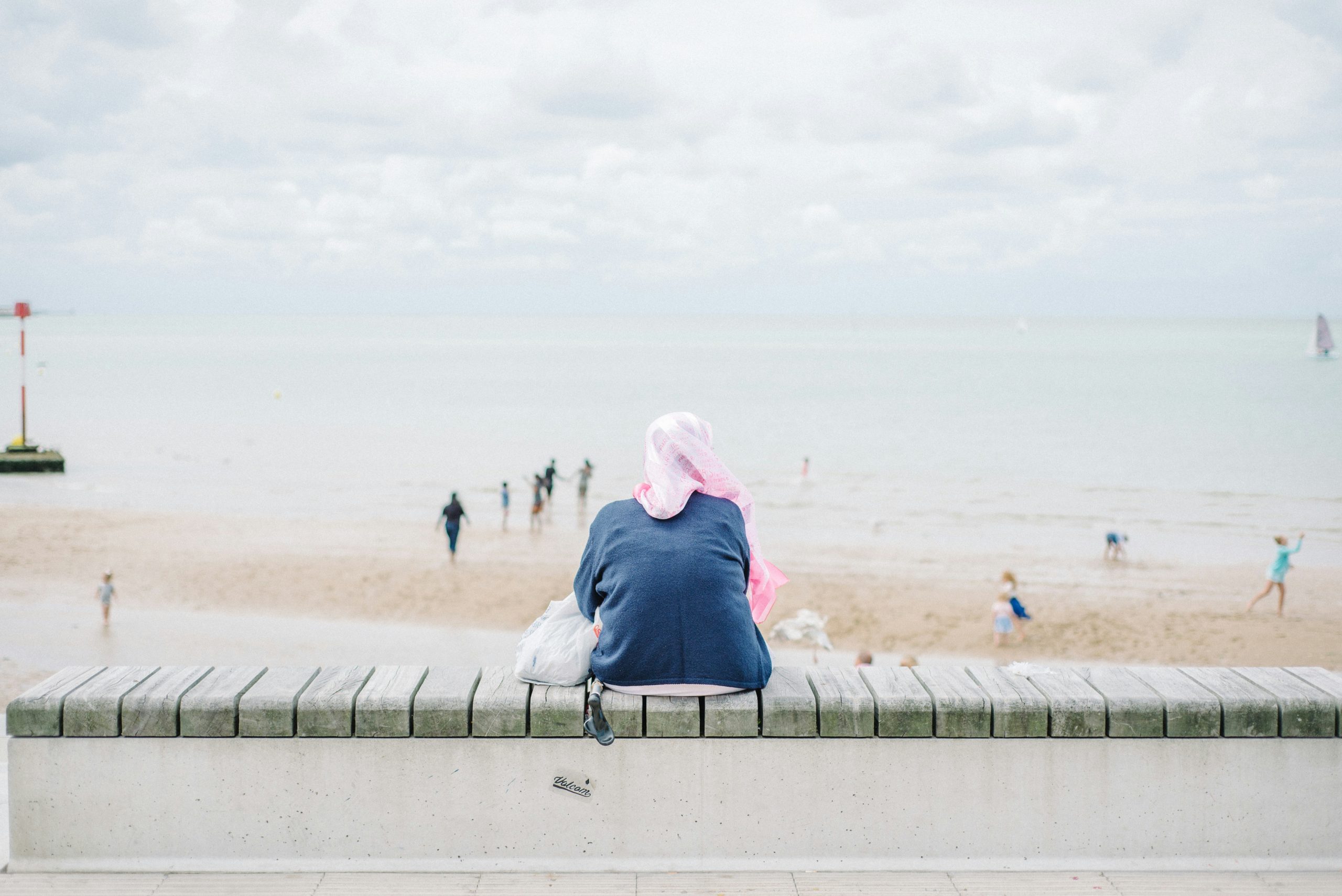 Person in a pink headscarf sitting on a concrete bench overlooking a calm Margate beach.