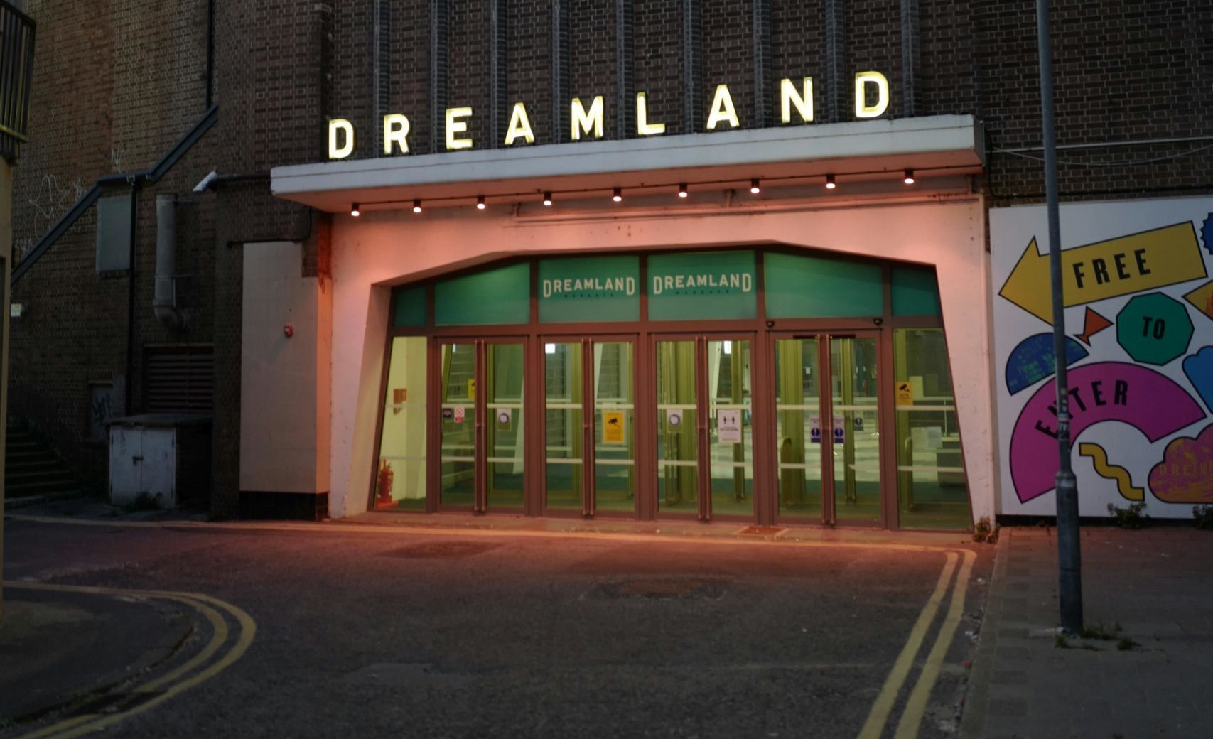 The front entrance to Dreamland Margate lit by evening lights with retro signage and a mural.
