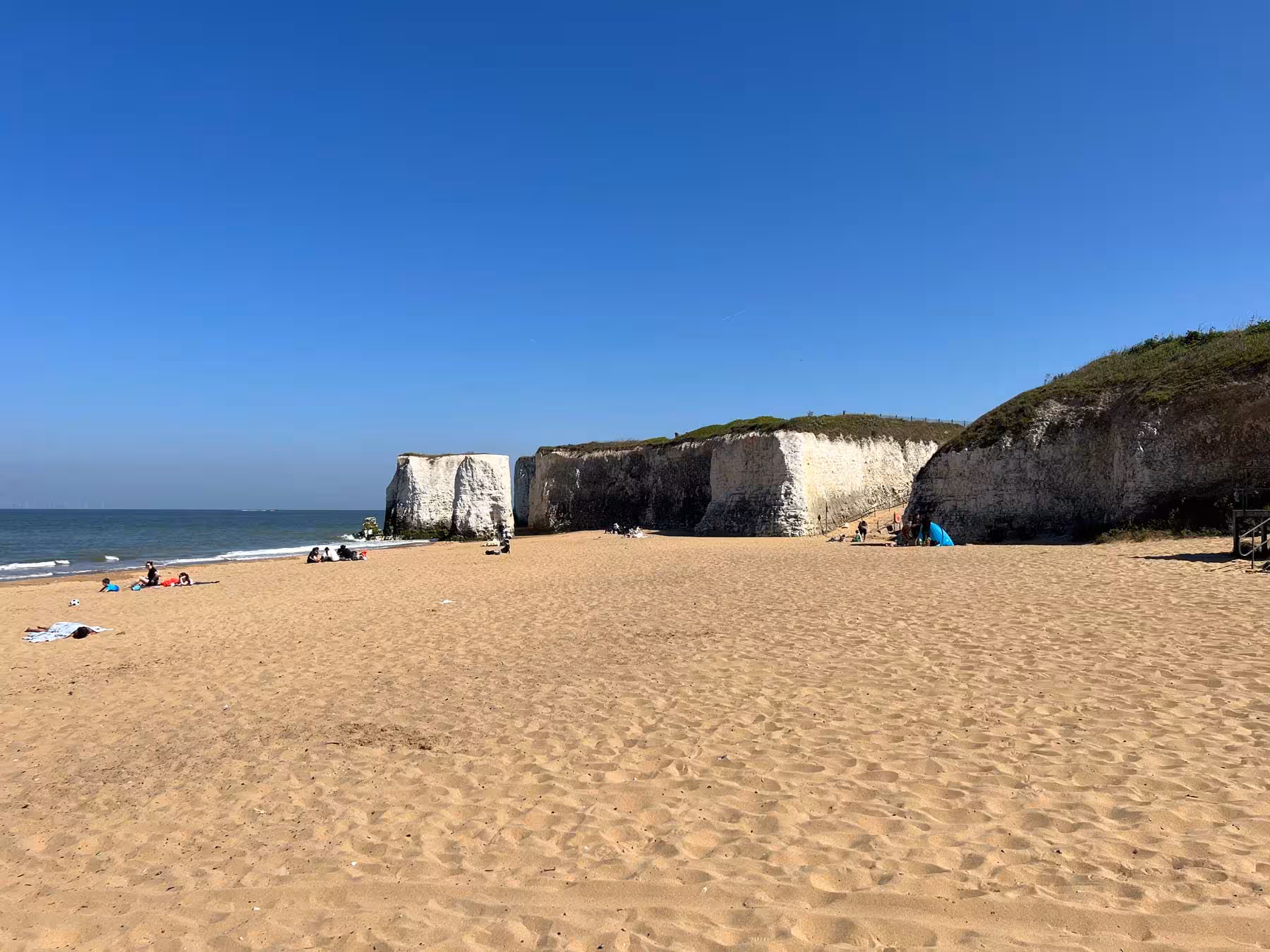 Wide sandy beach at Botany Bay with iconic white chalk cliffs under a clear blue sky.