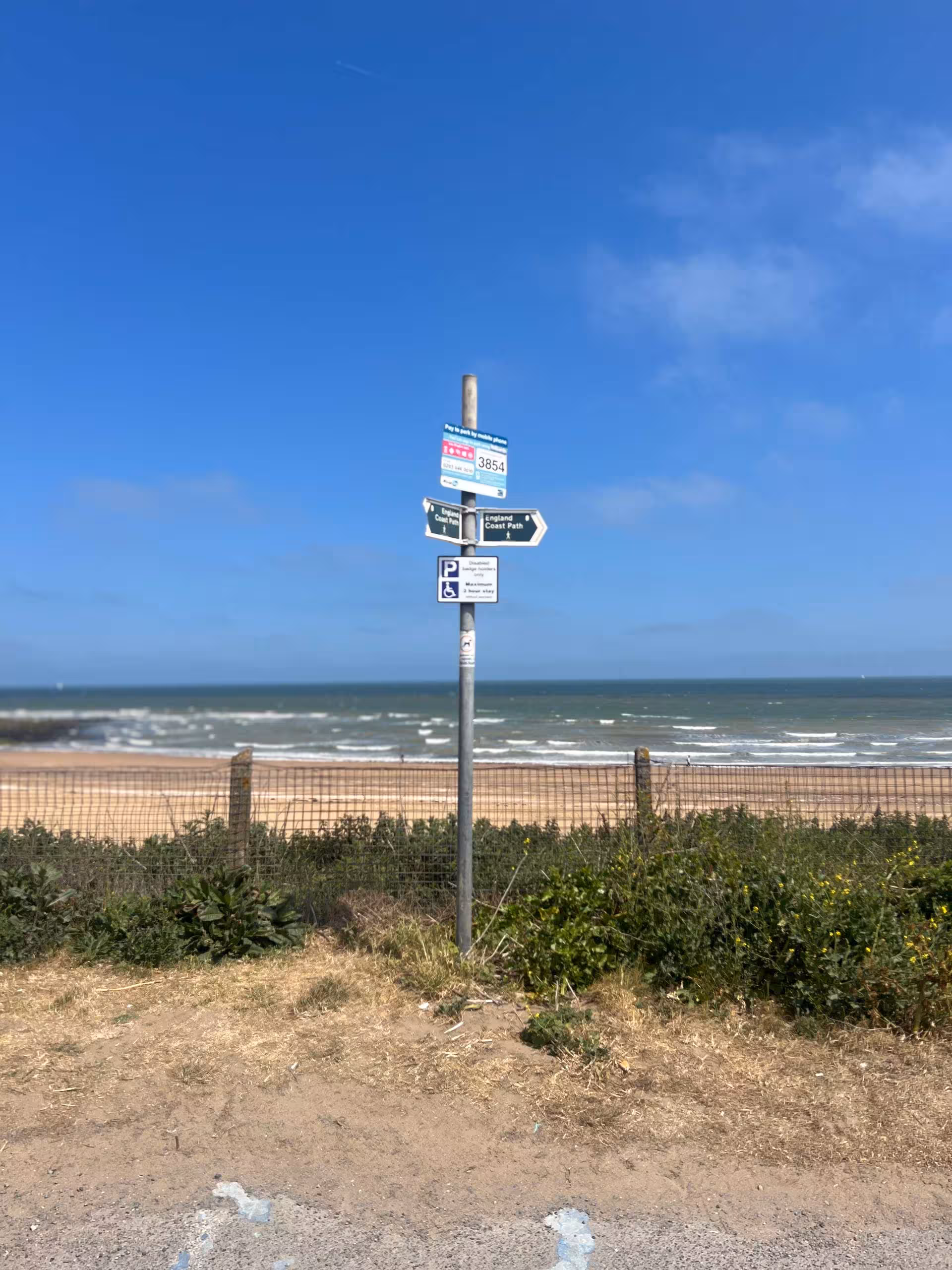 Coastal signpost against a backdrop of Joss Bay’s sandy beach and blue sea under a clear sky.