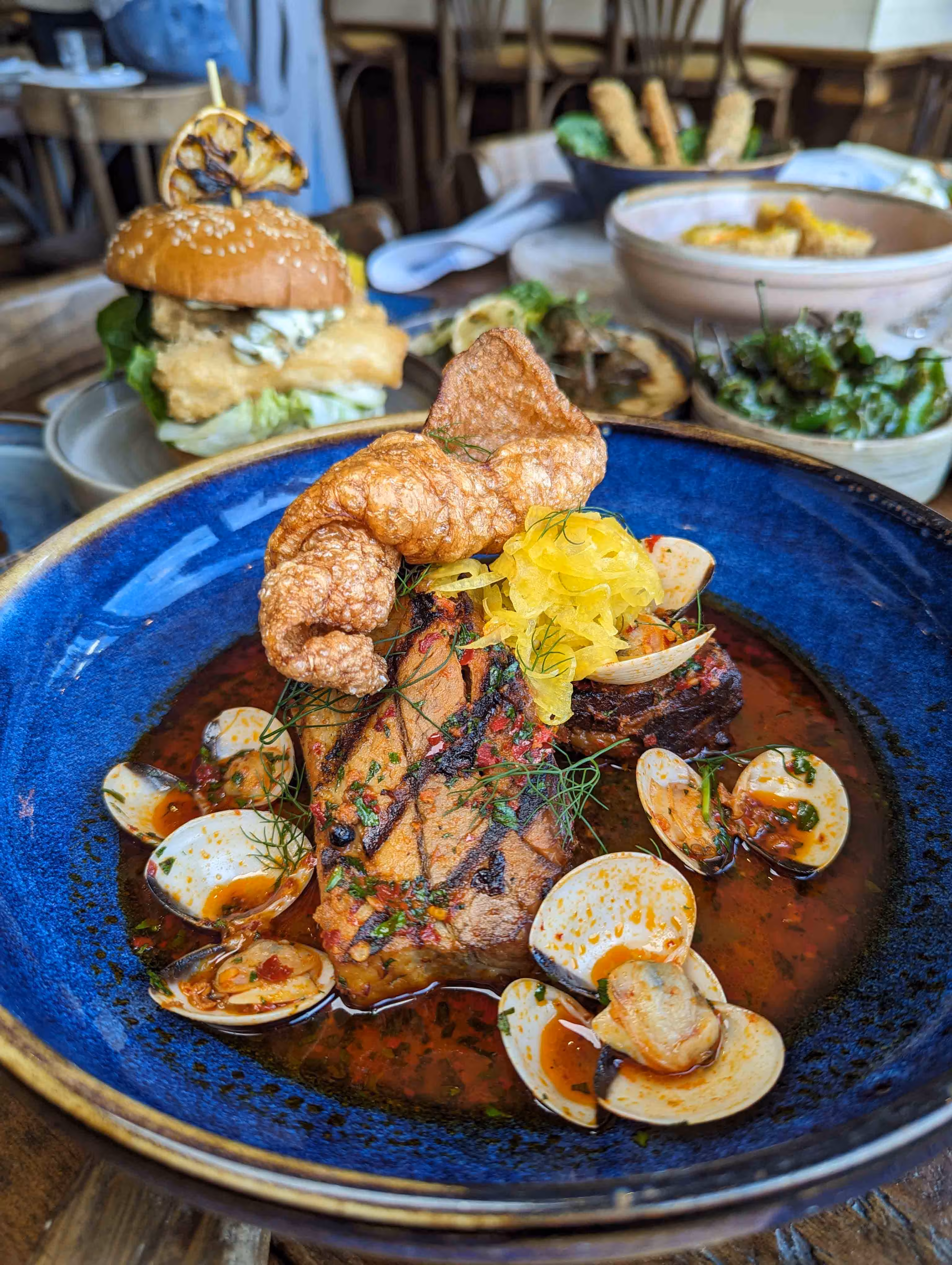 A dish of Slow-Cooked Pork with Clams, Pickled Fennel, and Crispy Crackling served in a vibrant blue bowl at Kebbells, Broadstairs.