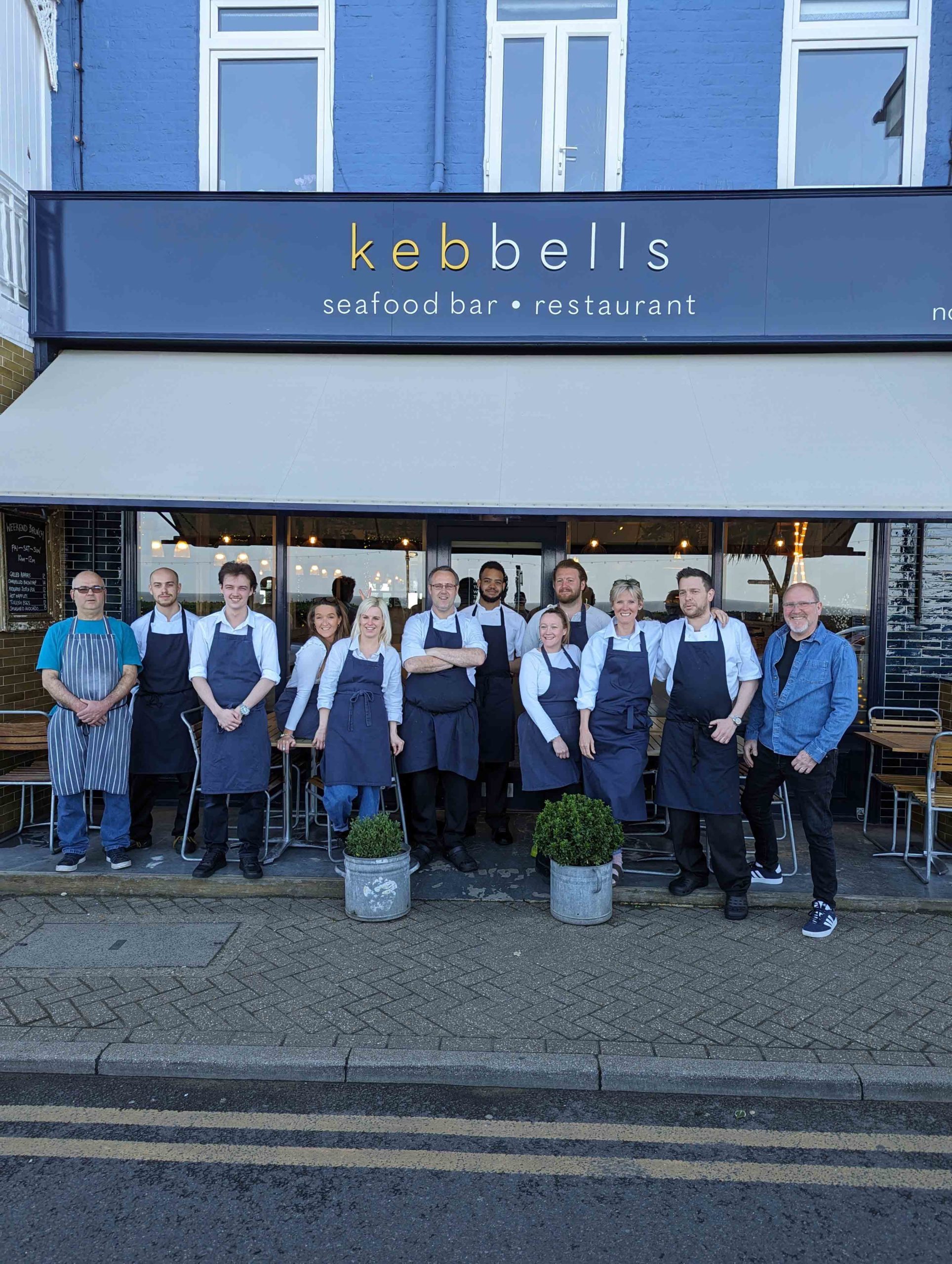 The team of chefs and staff at Kebbells seafood bar and restaurant in Broadstairs, standing proudly outside the restaurant in matching navy aprons.