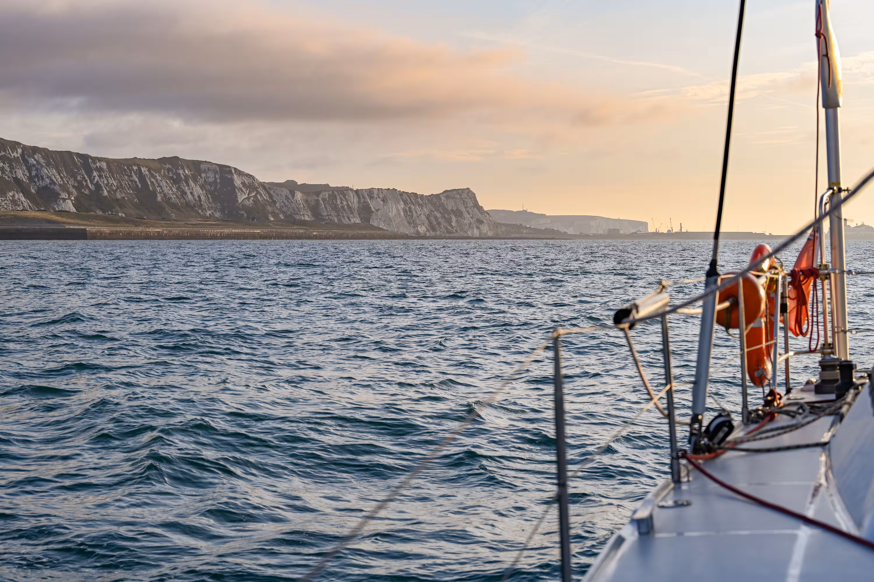 View of the White Cliffs of Dover from the deck of a sailing ferry at sunset.