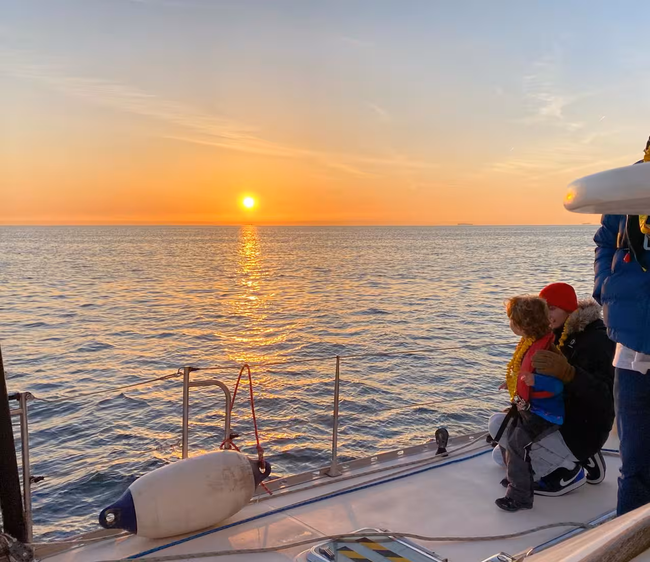 Family watching a serene sunset over the English Channel from the deck of a sailing ferry.